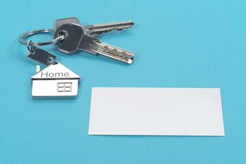 House symbol with silver keys and blank white business card on blue background. Real estate concept