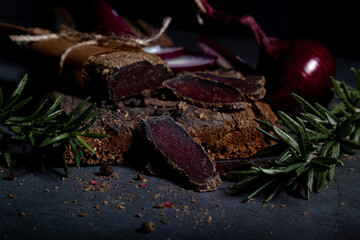 Salty, flavorful homemade basturma with aromatic spices and herbs on a dark background. Homemade recipes