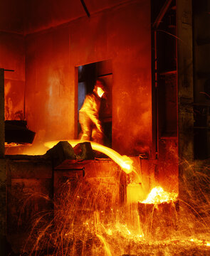 Obrero trabajando  hierro fundido en una fundidora industrial a altas temperaturas con equipo de protecci&oacute;n.