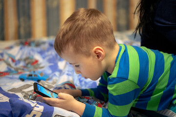 A little boy plays games on a smartphone. The boy lies and plays on the smartphone