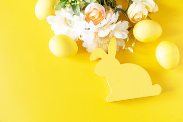 Fototapeta na wymiar Easter composition with colorful eggs, wooden bunny and spring flowers on yellow background. Copy space.