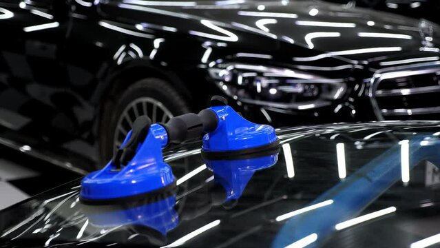 The glass of the car is a close-up in the room, taken with the help of professional suction cups. Bright illuminated car service with a car. The process of car repair.