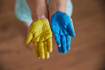 A cute child painted his hands in the colors of the Ukrainian flag
