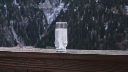 Anti Hangover Painkiller Medicine Effervescent Tablet Dropped into Glass of Warm Water Standing on Balcony Balustrade with Alps High Mountains Background