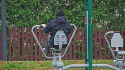 Caucasian Male in Warm Jacket Exercising Workout on Public Outdoor Gym Equipment