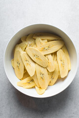  slices of ripe plantains in a white bowl, slices of yellow plantains for frying, process for making fried plantain