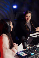 Female host and guest sitting at table with equipment while broadcasting radio program in recording...