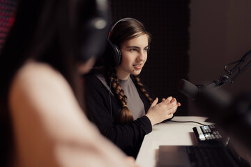 Young female with headphones sitting at table during podcast in recording studio