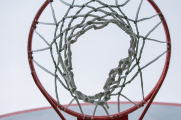 Looking up from underneath into a basketball net with an overcast sky in the background