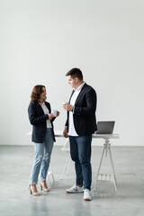 A man and a woman are talking over a cup of coffee in the office. A desktop with a laptop.