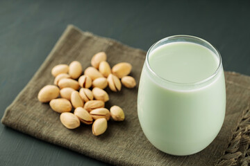 Glass of pistachio milk and pistachios on green linen napkin. Healthy vegetarian food and drink concept. Copy space