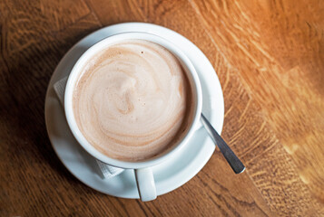 white cup with hot latte coffee on a wooden table. flatlay
