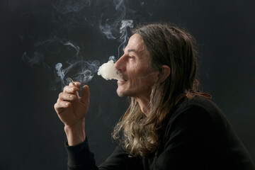 Obraz premium Studio portrait on black background of middle age man with long hair smoking cigarette