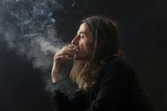Studio portrait on black background of middle age man with long hair smoking cigarette