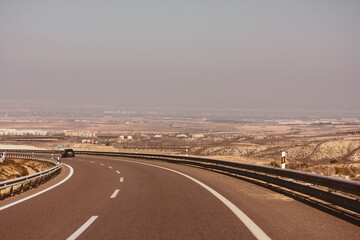 Fototapeta premium Curve road in a desert dry landscape. A bend of an asphalt road with excellent pavement, a dividing strip and a guardrail. Infrastructure, mobility, movement concept. Travel around the world, car trip