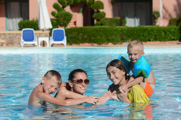 Fototapeta na wymiar Happy family play and swim in the pool, mother, siblings play on summer vacation, children smile and have fun in the pool.