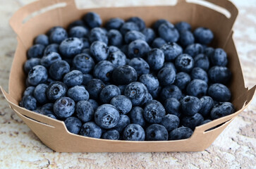 Fresh tasty blueberries in a cardboard container on an abstract background. Healthy food concept. Source of vitamins	
