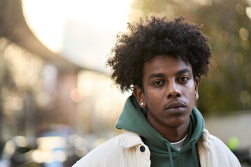 Cool sad lonely young African American guy standing at city street. Stylish serious pensive sensitive vulnerable ethnic rebel hipster gen z teen boy looking at camera outdoors, close up portrait. - obrazy, fototapety, plakaty