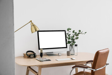 Modern workplace with computer, headphones and microphone near light wall