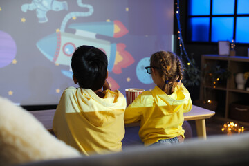 Little children in 3D glasses with popcorn watching cartoons on projector screen at home