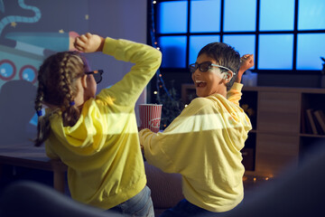 Little children in 3D glasses with popcorn watching cartoons on projector screen at home