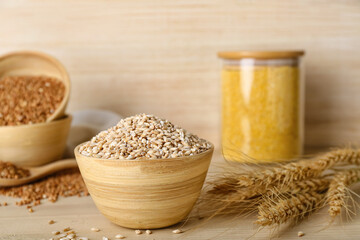 Bowl with pearl barley and spikelets on wooden background