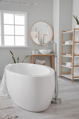 Stylish interior of bathroom with modern bathtub, sink and shelving units with accessories