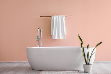 Obraz na płótnie Canvas Modern bathtub with towel and houseplant near pink wall