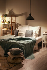 Interior of bedroom with cozy blankets on bed and glowing lamp late in evening