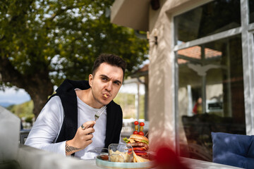 one young man sit at table eat burger and chips at restaurant outdoor