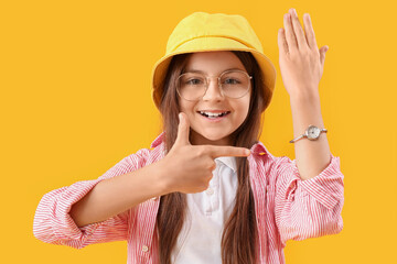 Little girl pointing at wristwatch on yellow background