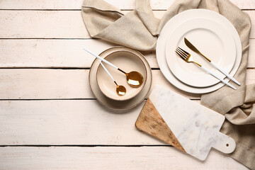 Board, dishes and set of cutlery on white wooden background