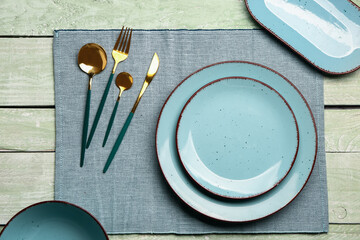 Blue tablecloth with plates and set of cutlery on green wooden background