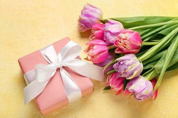 Gift box and beautiful tulip flowers on yellow background. Hello spring