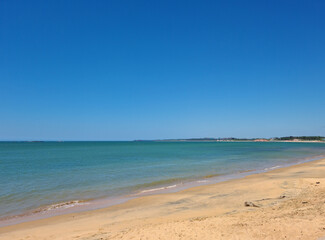 Image by the beach with clear, smooth sand and dark blue sea