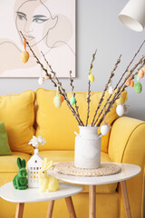 Vase with willow branches, Easter eggs and rabbits on tables in living room