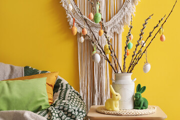 Vase with willow branches, Easter eggs and rabbits on table in living room