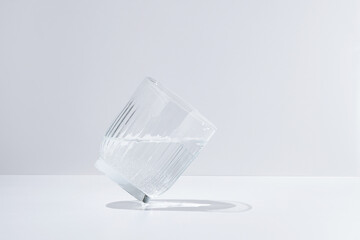 Tilted clear glass of sparkling water on white isolated background in daylight. Elegant image for...