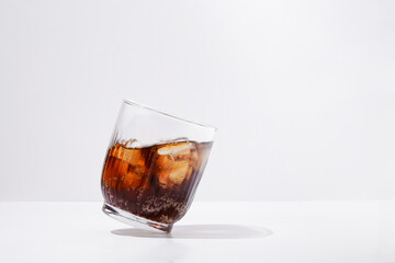Tilted transparent glass with cola wave and ice on white isolated background on daylight. Place for your design - obrazy, fototapety, plakaty