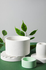 Plaster podiums and ficus branches on green table against grey background