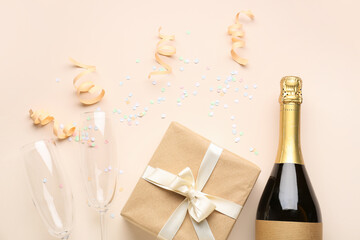 Bottle of champagne, gift box, glasses and serpentine on beige background