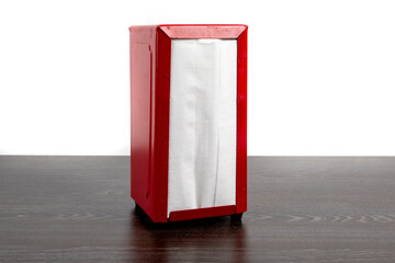 A red square restaurant napkin holder on a dark tabletop reminiscent of a British telephone booth