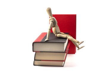 A wooden artist's mannequin sitting a pile of books isolated on white