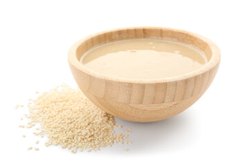 Wooden bowl with tasty tahini and sesame seeds on white background