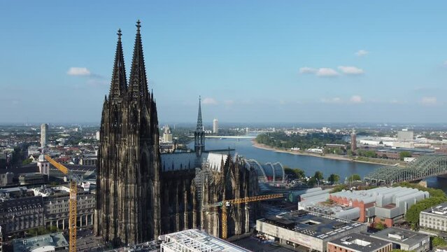 german cologne cathedral shot from above by drone fly around the building with construction crane in front and rhine river and landskape of city in the background on sunny summer day