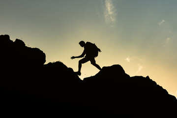 Hiker silhouette hiking up rocky mountain cliff. Success, goal setting.  - obrazy, fototapety, plakaty
