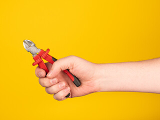 A hand holds a side cutter. No face, yellow background.
