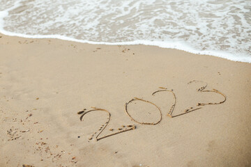 Happy New Year 2023, lettering on the beach with wave and clear blue sea. 
