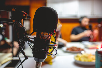 Closeup of professional microphone in scissor arm stand with blurred people recording program with...
