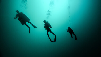 Fototapeta na wymiar silhouette of a technical dive guide and two tourists. cenote diving, unrecognizable people